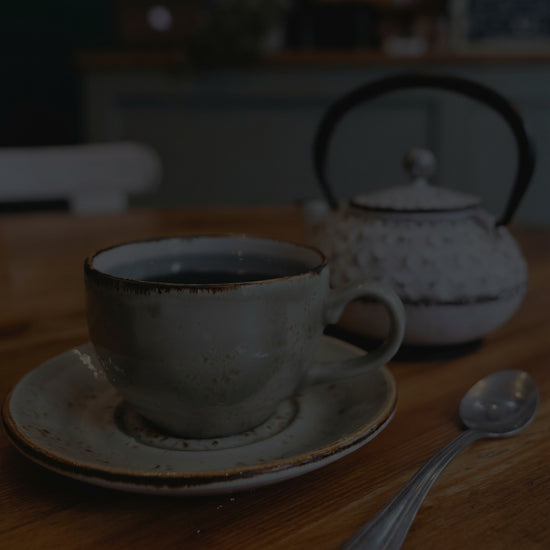 Tea cup, teapot, and spoon on a wooden table with a blurred cafe background